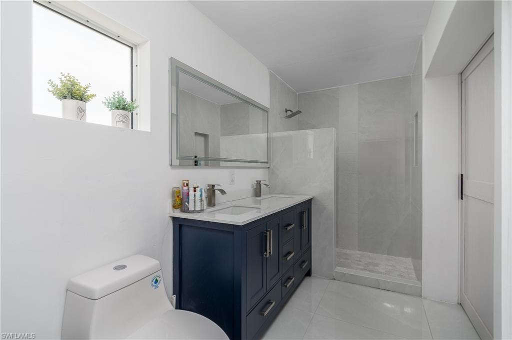Dual sink vanity with dark wood-finish cabinetry, a large mirrored medicine cabinet, a tiled shower enclosure, and a high window