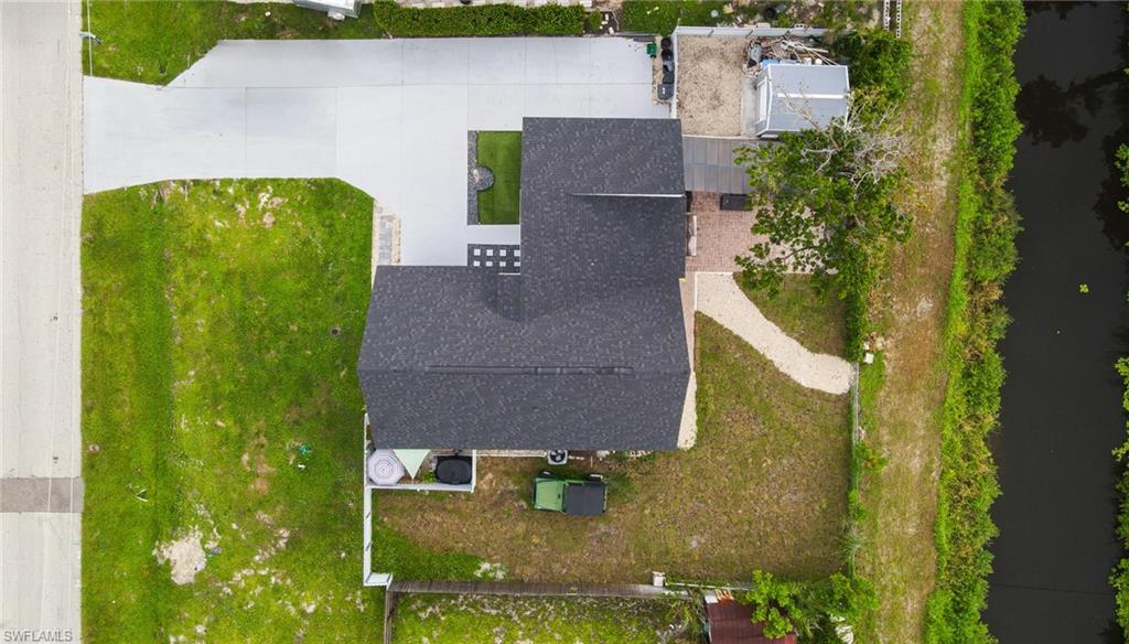 Asphalt shingle roof, concrete driveways, brick paver patio, gravel pathway, and adjacent waterway