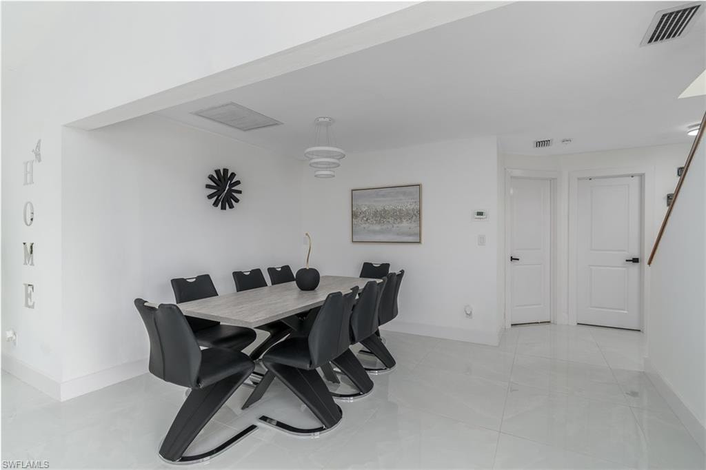 Open-concept dining area featuring white walls, large format floor tiling, a multi-tiered pendant light fixture, and two panel doors with dark hardware