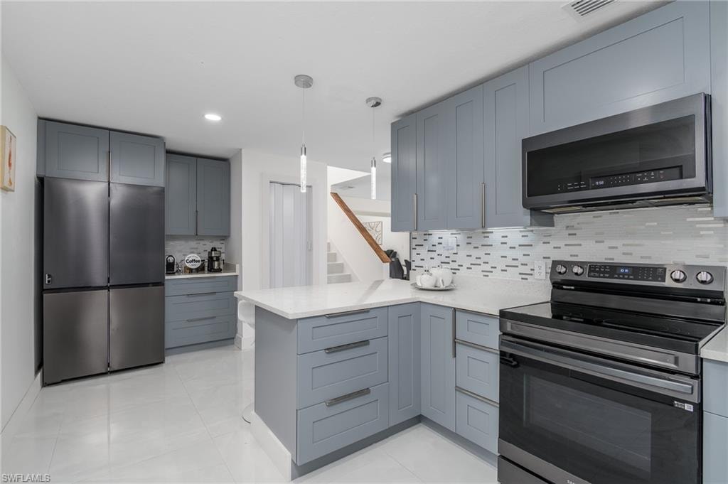 Kitchen featuring gray shaker-style cabinetry, white countertops, tile backsplash, and stainless steel appliances