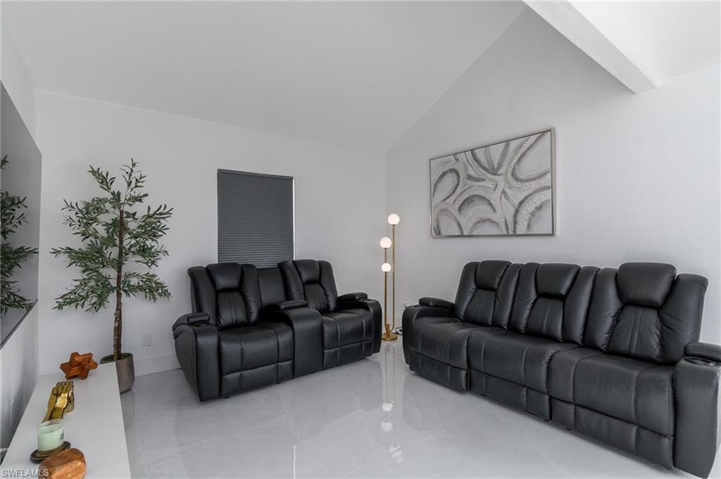 Modern living room showcasing dual black leather reclining sectionals with integrated cup holders, polished light-reflective flooring, vaulted ceiling with recessed lighting, and accent wall art