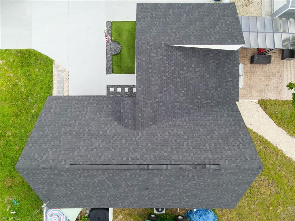 Asphalt shingle roofing, paved driveway, artificial turf landscaping, paver patio, and gravel pathway
