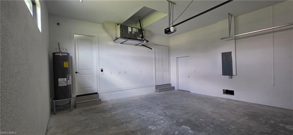 Concrete flooring with a white painted wall finish, featuring two entry doors, a built-in water heater, and an overhead garage door mechanism