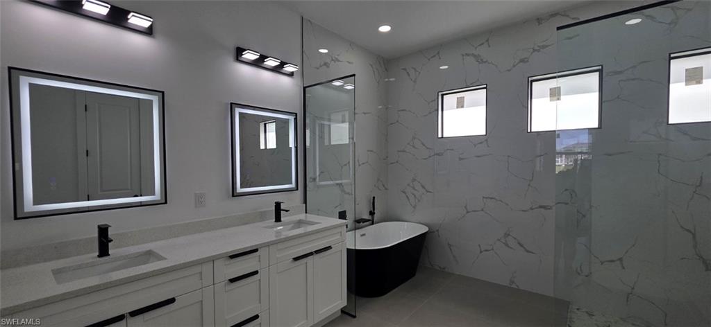 Spa-inspired primary bathroom featuring dual vanities with white cabinetry and integrated sinks, LED-backlit mirrors, polished stone countertops, and matte black hardware