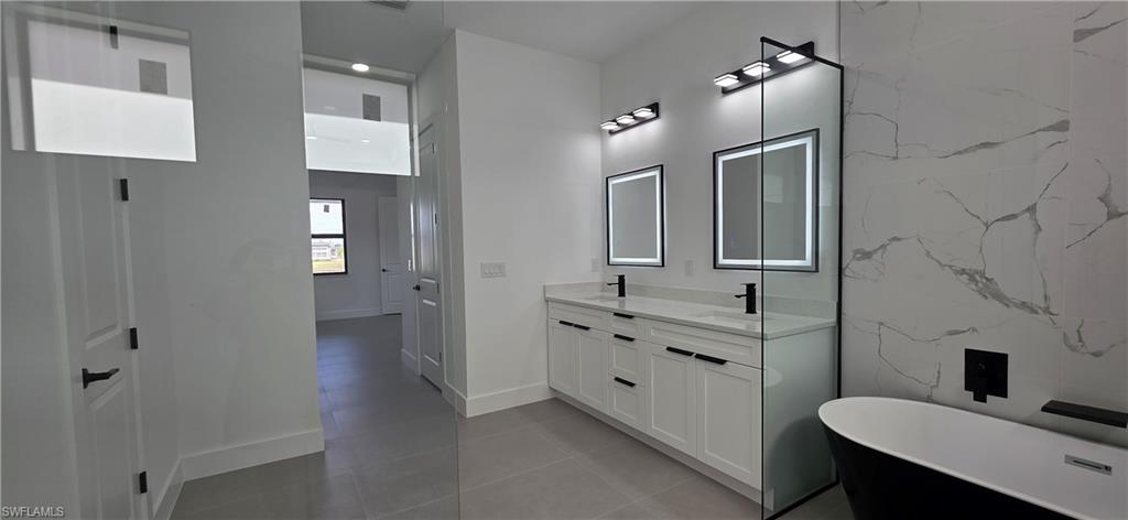 Bathroom featuring a dual vanity, back-lit mirrors, a freestanding soaking tub, and a glass-enclosed shower with a tiled accent wall