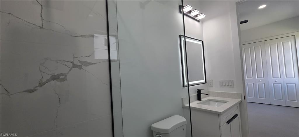 Full-height tile shower surround, vanity with stone countertop, matte black faucet, and illuminated mirror
