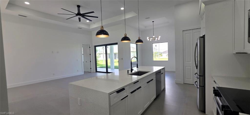 Open-concept layout featuring a kitchen island with built-in sink, stainless steel appliances, and a tray ceiling with a modern ceiling fan