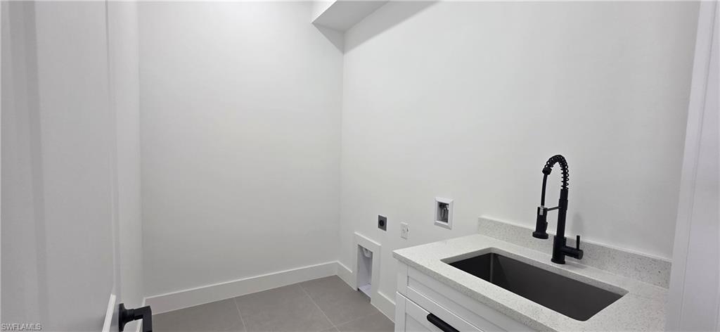Utility room featuring a utility sink with a matte black pull-down faucet, light-toned countertop, white cabinetry with black hardware, and gray floor tiling