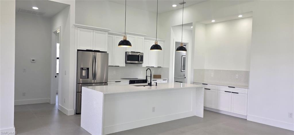 Open-concept kitchen featuring an oversized island, stainless steel appliances, white cabinetry, and recessed lighting