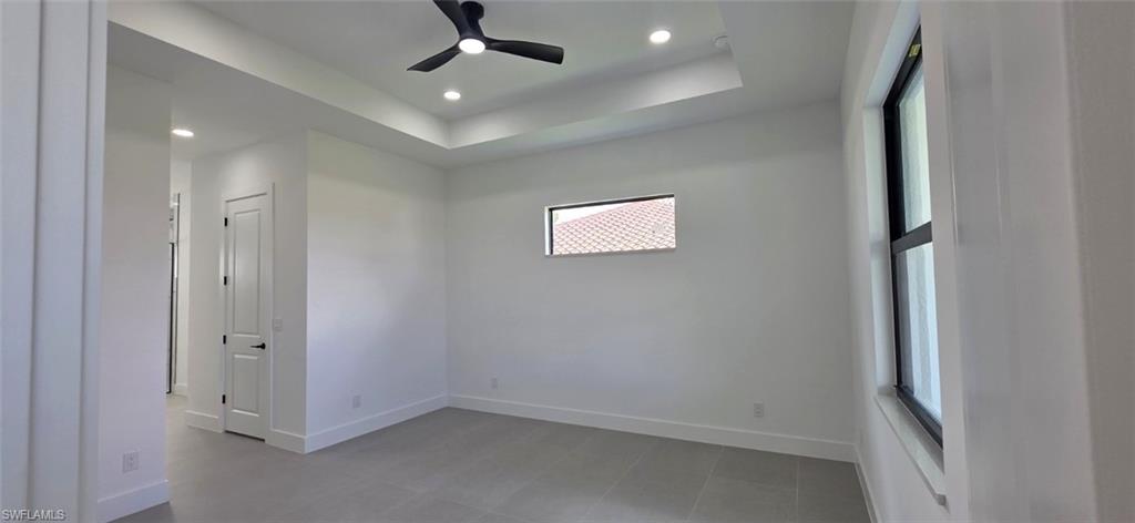 Tray ceiling with recessed lighting, ceiling fan, grey tile flooring, white interior doors with black hardware, and large windows