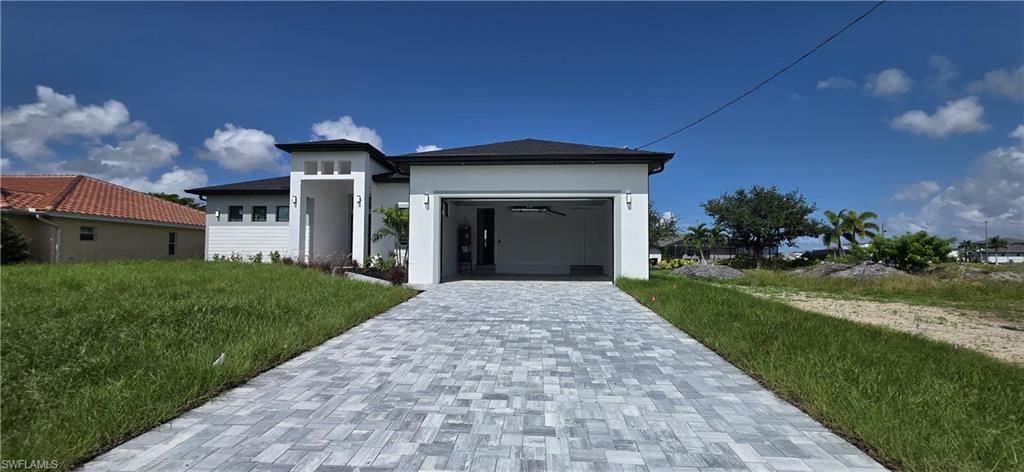 Contemporary exterior with a dark roof and white stucco finish, featuring an integrated garage and a paver driveway