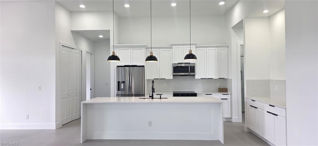 Kitchen featuring a large island, white cabinetry, stainless steel appliances, and pendant lighting