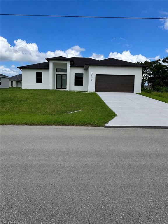 Contemporary stucco exterior with a dark shingle roof, expansive concrete driveway, and a prominent front entry with dark-framed double doors