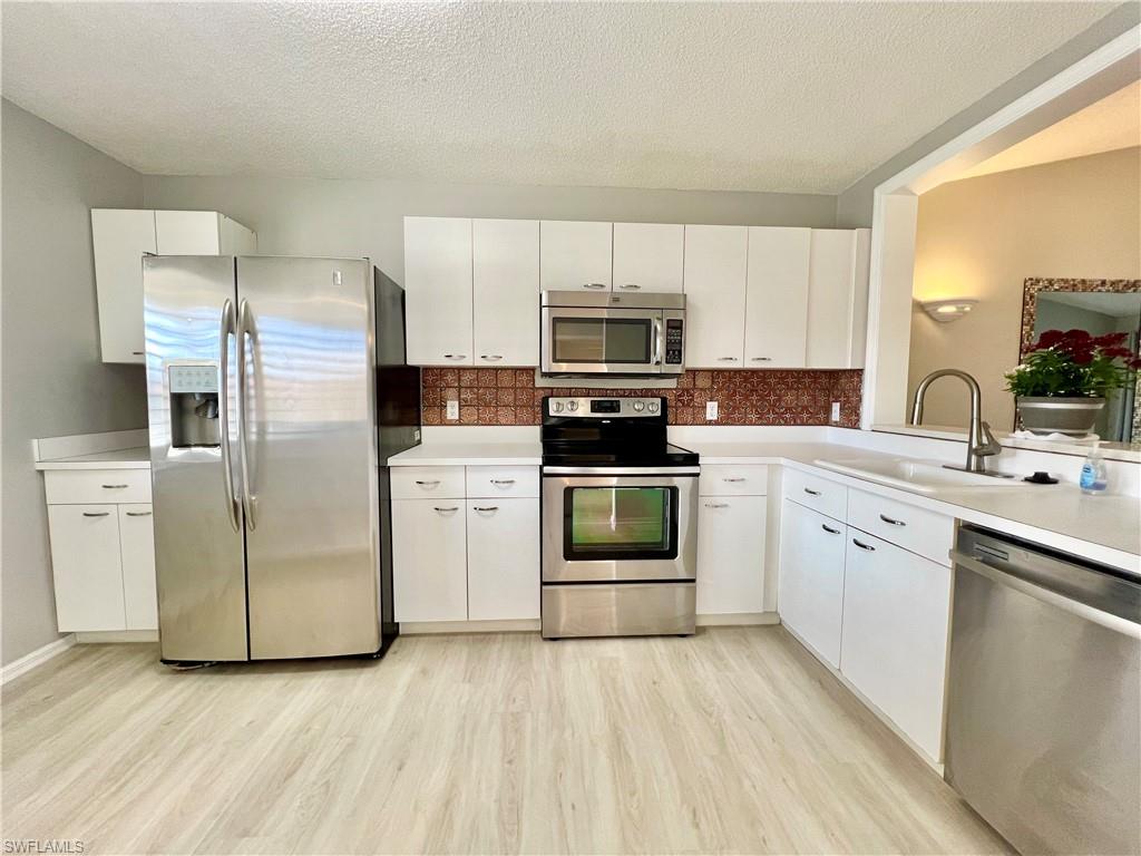 Kitchen with appliances with stainless steel finishes, a sink, light wood-style flooring, decorative backsplash, and a textured ceiling