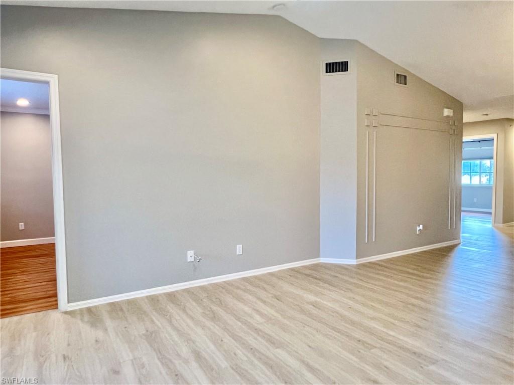 Empty room featuring light wood-type flooring, vaulted ceiling, and baseboards
