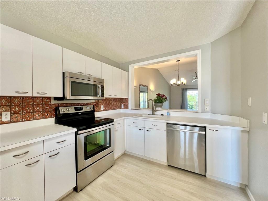Kitchen with appliances with stainless steel finishes, a sink, decorative backsplash, light countertops, and white cabinetry