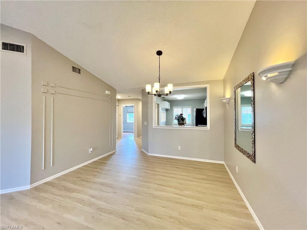 Unfurnished dining area with a chandelier, lofted ceiling, light wood finished floors, baseboards, and a textured ceiling