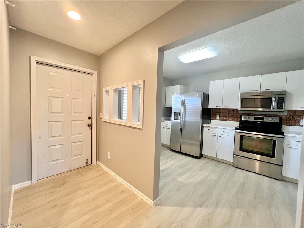 Kitchen with stainless steel appliances, light wood-style flooring, white cabinetry, backsplash, and baseboards