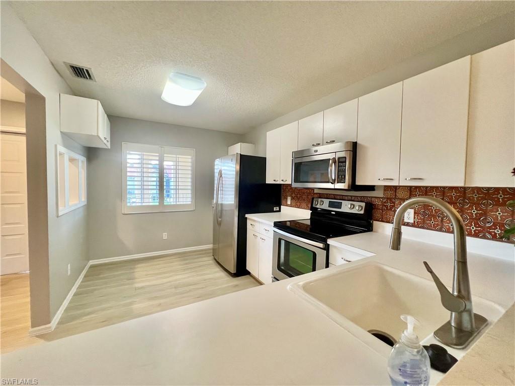 Kitchen with stainless steel appliances, a sink, light wood finished floors, tasteful backsplash, and white cabinets
