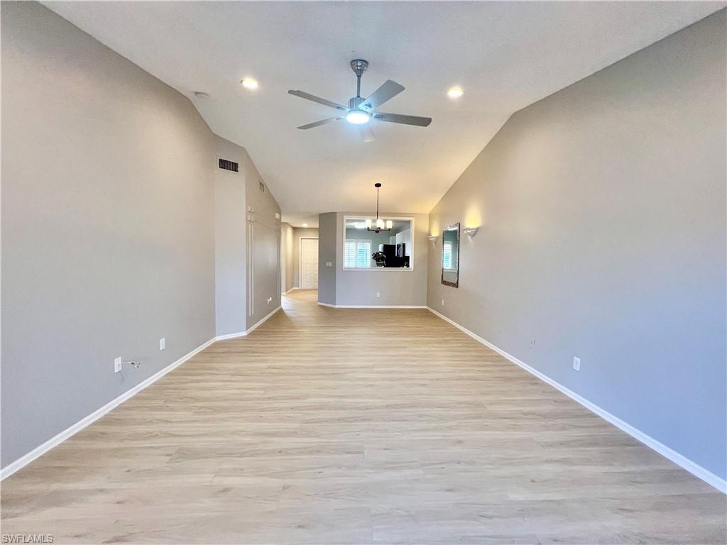 Unfurnished room featuring a chandelier, a ceiling fan, light wood-style flooring, vaulted ceiling, and recessed lighting