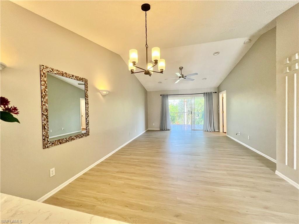 Unfurnished living/dining room with vaulted ceiling, light wood-type flooring, a chandelier, a ceiling fan, and baseboards