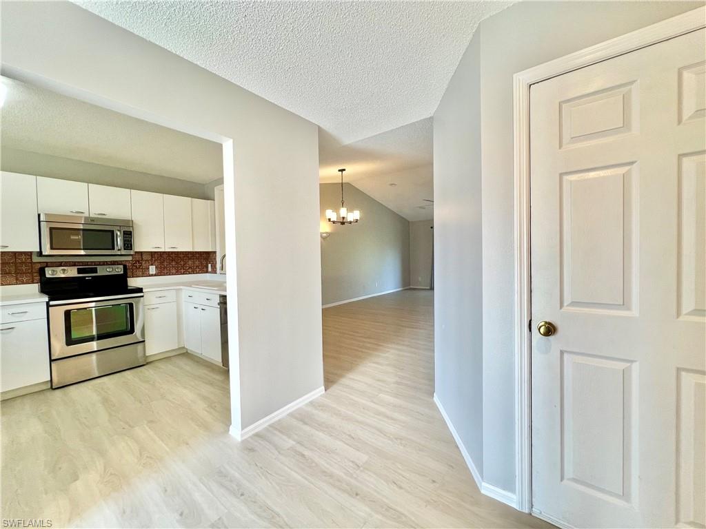 Kitchen featuring stainless steel appliances, light wood-type flooring, a chandelier, white cabinets, and baseboards
