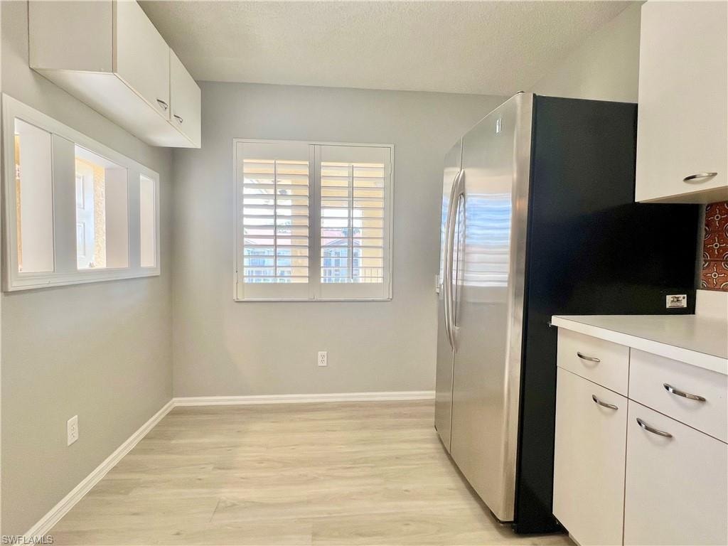 Kitchen featuring freestanding refrigerator, light wood-style floors, light countertops, and white cabinets