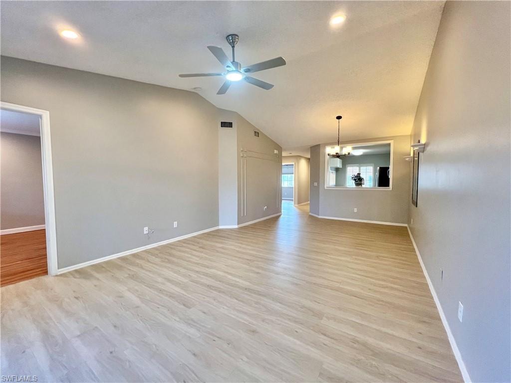 Unfurnished living room with a chandelier, ceiling fan, light wood-style flooring, lofted ceiling, and baseboards