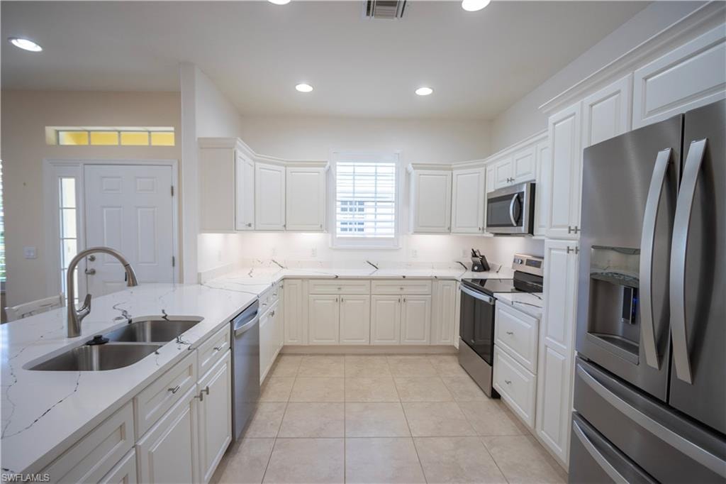 Well-appointed kitchen featuring white cabinetry, stainless steel appliances, a double basin sink, stone countertops, and recessed lighting