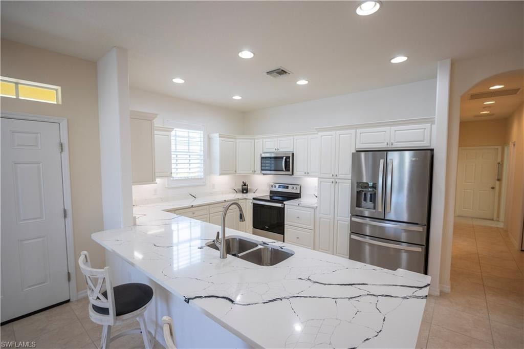 Kitchen featuring a large island with sink, white shaker-style cabinetry, stainless steel appliances, recessed lighting, and a transom window