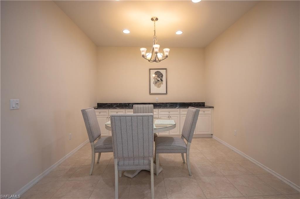 Recessed ceiling lighting, a central chandelier, tiled flooring, white cabinetry with dark countertops, and a built-in buffet