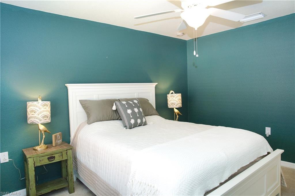 White paneled headboard and footboard, ceiling fan with integrated lighting, teal painted walls, and carpeted flooring