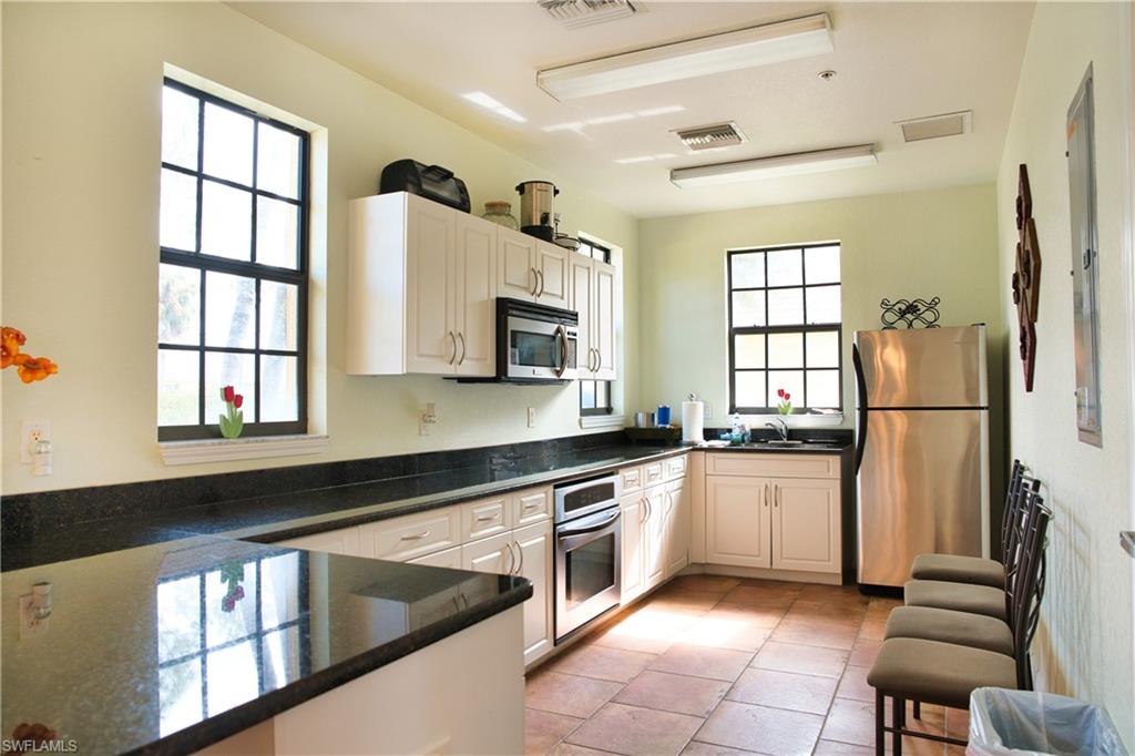 White cabinetry, dark stone countertops, stainless steel appliances, tiled flooring, and multiple windows