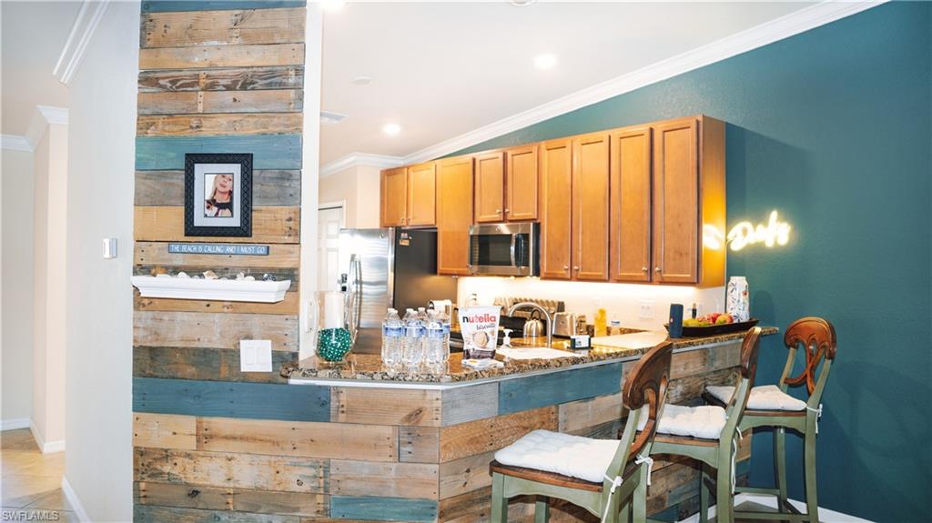 Reclaimed wood-finish accent wall, built-in breakfast bar with stone-finish countertop, wood cabinetry, recessed lighting, and stainless steel appliances