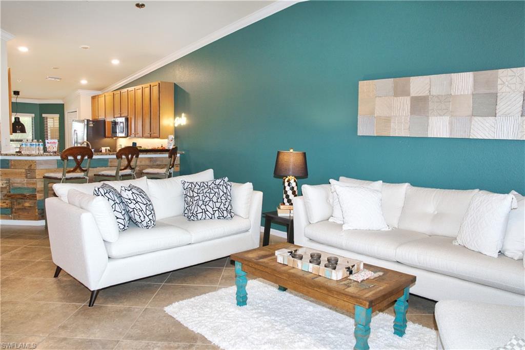 Open-concept living area with tile flooring and a kitchen featuring wood-finish cabinetry, stainless steel appliances, and a breakfast bar with a decorative wood panel facade
