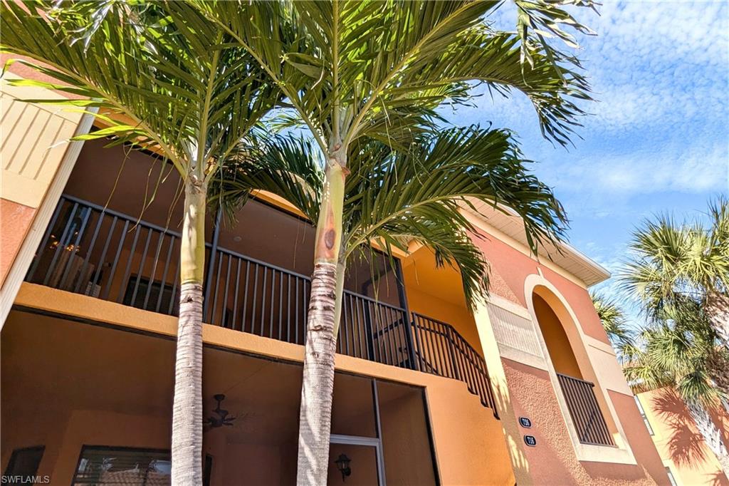 Multi-story building featuring balconies with black railings, exterior arched architectural details, and mature palm trees