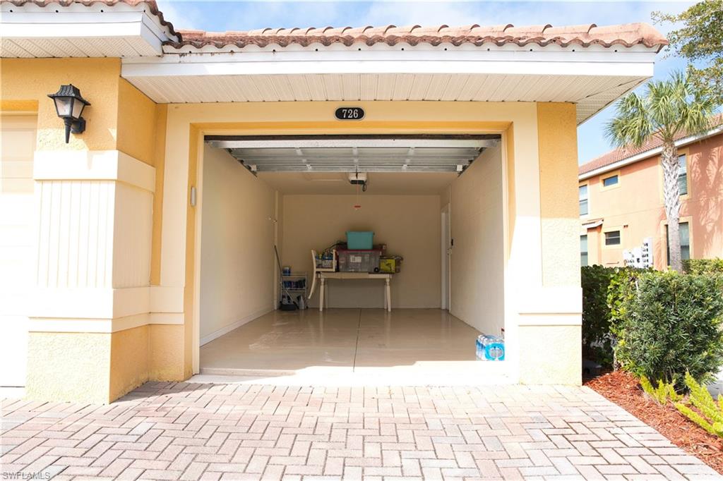 Stucco exterior with a tiled roof, open garage with concrete flooring, and a paver driveway