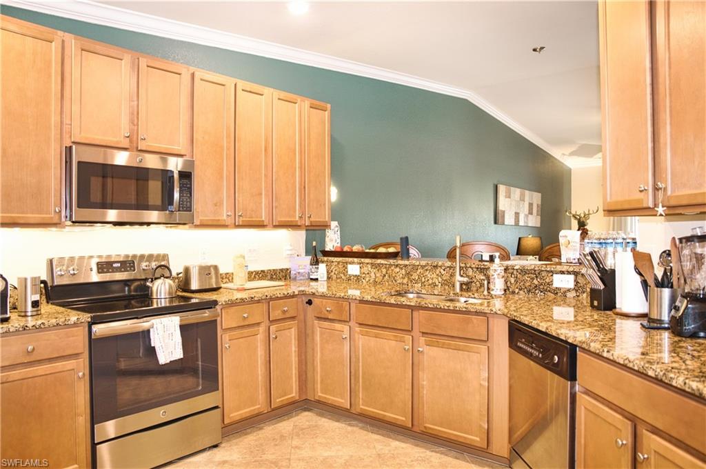 Kitchen featuring wood cabinetry, stainless steel appliances, granite countertops, and tile flooring