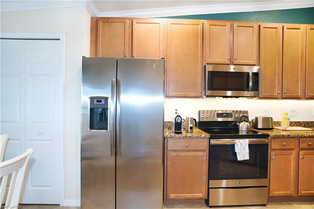 Stainless steel side-by-side refrigerator, stainless steel microwave, stainless steel range, wood-finish cabinetry, and speckled countertops