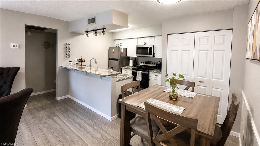Kitchen with granite countertops, stainless steel appliances, wood-finish flooring, and white cabinetry