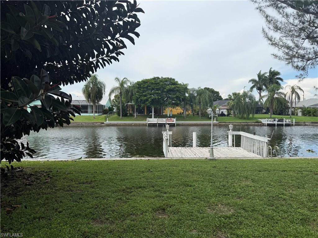 Waterfront property with a private dock featuring white railings and integrated lighting, alongside a manicured lawn