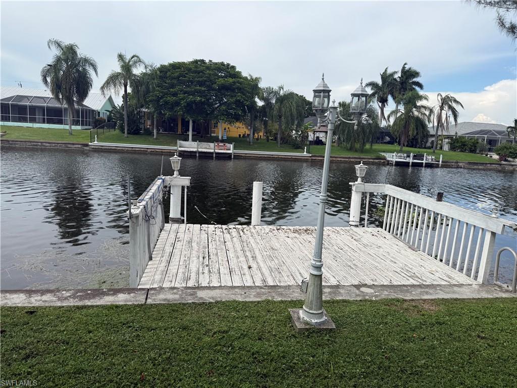 Waterfront property featuring a private wooden dock, concrete seawall, and mature landscaping