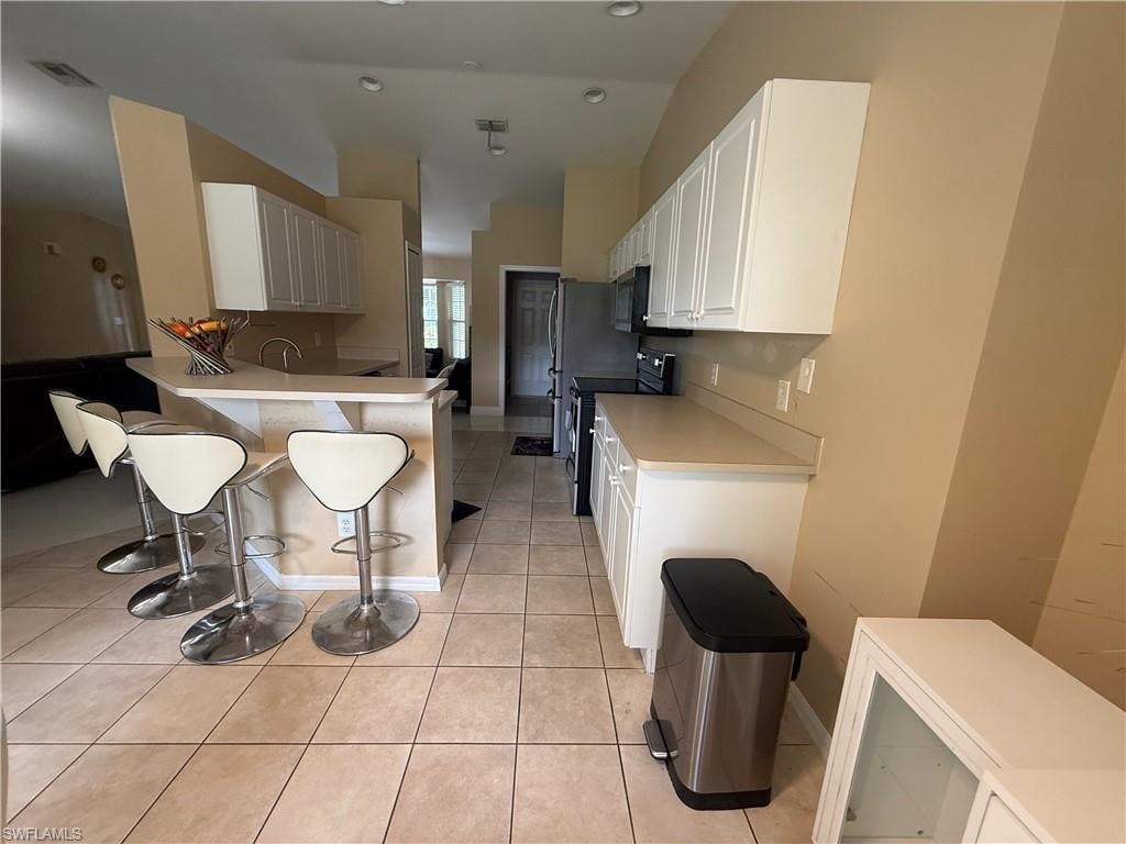 Kitchen featuring an integrated breakfast bar, ample white cabinetry, tile flooring, stainless steel appliances, and vaulted ceilings