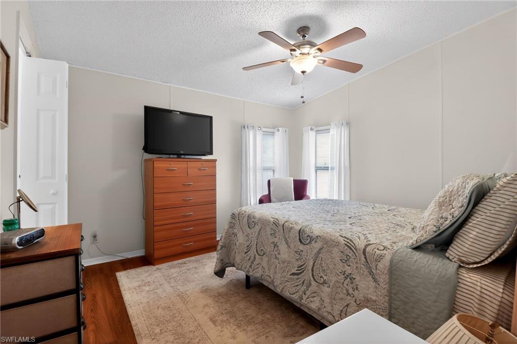 Bedroom with wood-finish flooring, two windows, and a ceiling fan with integrated lighting