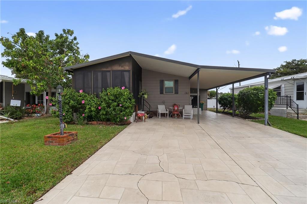 Front exterior featuring a screened porch, covered carport, stamped concrete driveway, mature landscaping, and a manicured lawn