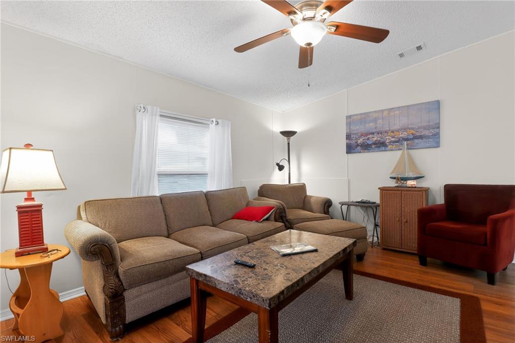 Living area featuring wood-finish flooring, a ceiling fan with integrated lighting, and a window with blinds