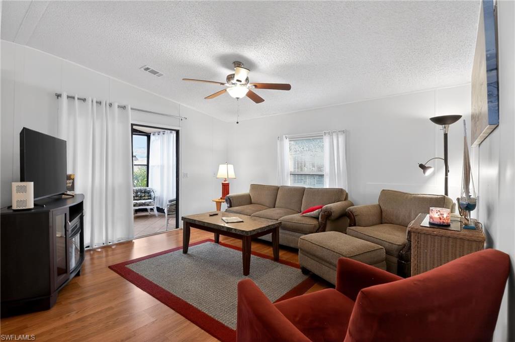 Spacious living area featuring wood-finish flooring, a ceiling fan, and white vertical wall paneling
