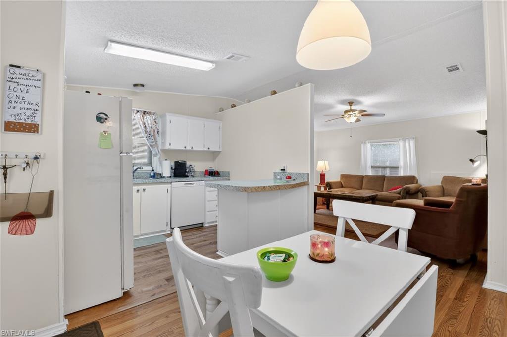 Kitchen featuring wood-finish flooring, white cabinetry, a built-in dishwasher, and a breakfast bar with a solid surface countertop