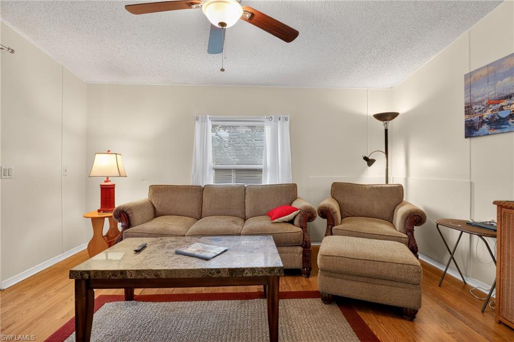 Living area featuring wood-finish flooring, a ceiling fan with integrated lighting, and a window with blinds