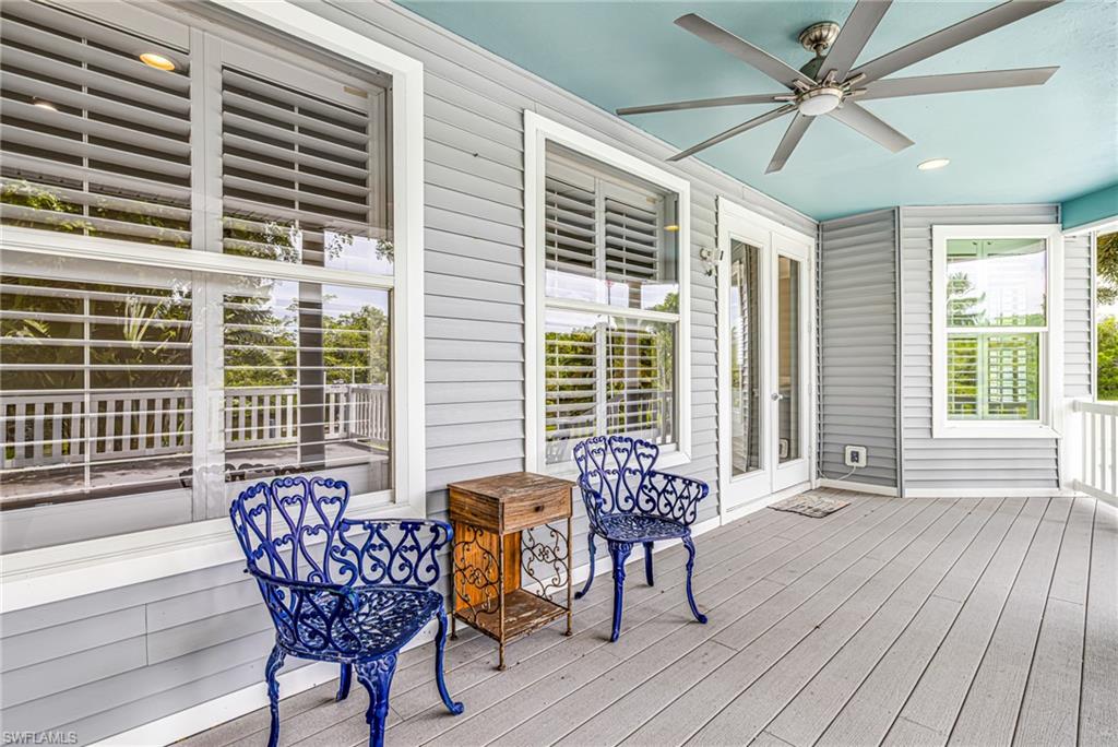 Covered outdoor porch featuring a vibrant blue ceiling, a large ceiling fan with integrated lighting, plank flooring, and multiple windows with plantation shutters